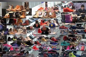 das Schaufenster eines Schuhladens in dem mitndestens 30 verschiedenen Schuhe ausgestellt sind und zwischen Turnschuhen und Winterstiefeln sieht man einige Baseballmützten