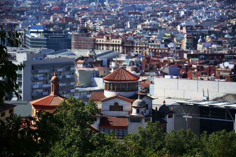 Blick auf Barcelona vom Gaudi Park aus, im Vordergrund grüne Bäume und danach Gebäude so weit das Auge reicht