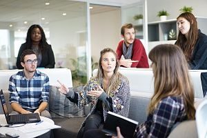 mehrere Personen die im Gemeinschaftsbereich eines Gebäudes sitzen und stehen und diskutieren