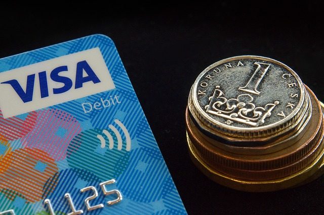 links ist die hälfte einer Visa Kreditkarte zu sehen und rechts daneben ein Turm aus tschechischen Münzen