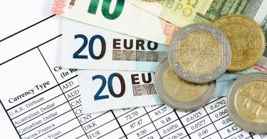 in einem Fächer liegen zwei zwanzig euro scheine ein zehn euro Schein und ein fünf euro schein mit Münzen darauf auf einer Tabelle mit Wechselkursen verschiedener Währungen