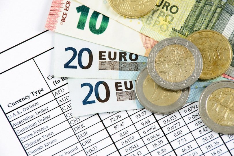 in einem Fächer liegen zwei zwanzig euro scheine ein zehn euro Schein und ein fünf euro schein mit Münzen darauf auf einer Tabelle mit Wechselkursen verschiedener Währungen