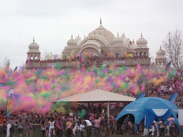 ein Hindutempel mit einer Menschenmenge drum herum und in der Luft schweben verschiedenfarbige Pulver die die Leute in die höhe geworfen haben