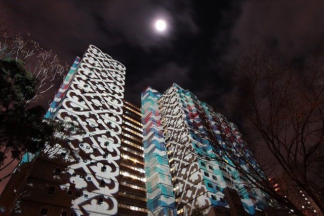 ein Hochhaus auf dem verschiedene Muster projiziert werden, es ist Nacht und genau darüber sieht man den Vollmond