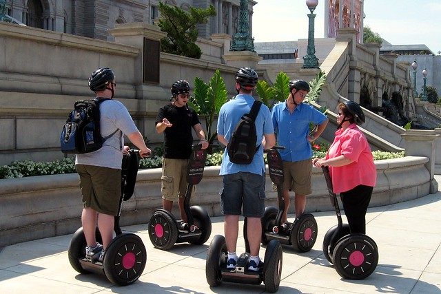 eine Familie vor einem Gebäude die Information darüber von einem Führer bekommen, alle stehen auf einem Segway und haben einen schwarzen Helm auf