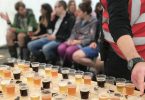 Bierdegustation auf dem Bierfestival, mehrere Leue sitzen in Stuhlreihen vor einem Tisch mit kleinen bechern die mit verschiedenen Biersorten gefüllt sind
