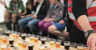 Bierdegustation auf dem Bierfestival, mehrere Leue sitzen in Stuhlreihen vor einem Tisch mit kleinen bechern die mit verschiedenen Biersorten gefüllt sind