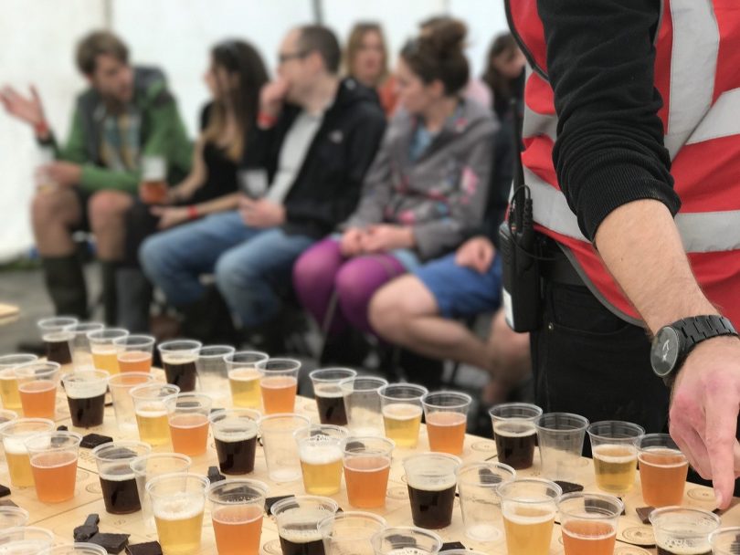 Bierdegustation auf dem Bierfestival, mehrere Leue sitzen in Stuhlreihen vor einem Tisch mit kleinen bechern die mit verschiedenen Biersorten gefüllt sind