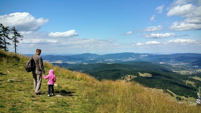 ein mann mit einem kleinen Kind die sich die Hände halten und von einem Berg ins Tal sehen