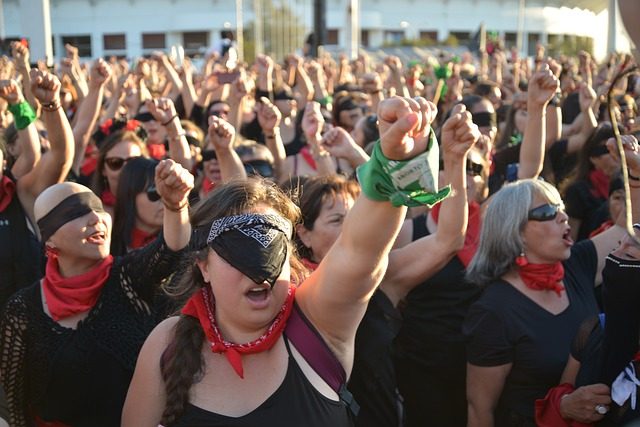 Frauenstreik, alle Frauen halten ihre linke Faust in die Luft, viele haben sich ihre augen mit einem schwarzen Tuch oder einer Sonnenbrille verdeckt und alle sind schwarz gekleidet