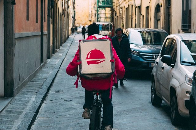 eine Person auf einem Fahrrad die durch die Straße fährt und hinten einen Rucksack mit essen trägt 