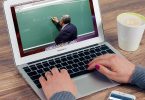 eine Person die an einem Laptop etwas schreibt während sie ein video von einem Lehrer sieht der eine mathematische Operation erklärt
