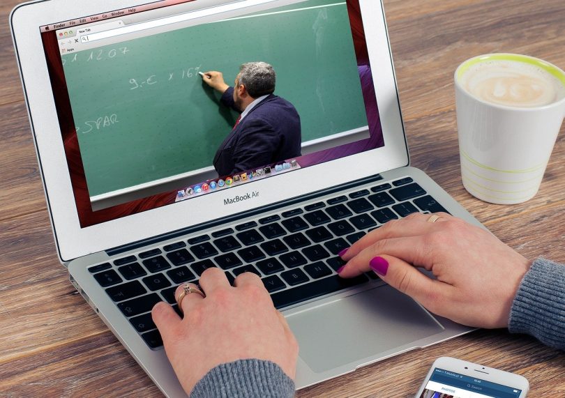 eine Person die an einem Laptop etwas schreibt während sie ein video von einem Lehrer sieht der eine mathematische Operation erklärt