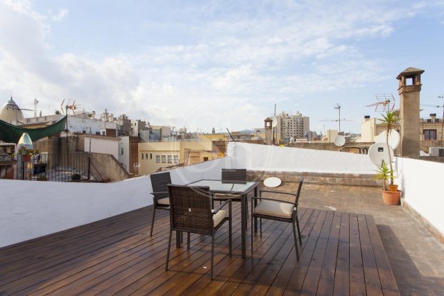 Wohnung in Ciutat Vella, zu sehen ist die Dachterrazze mit Holzboden, ein viereckiger Tisch und vier schwarze Stühle