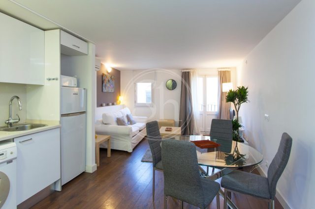 Wohnung an der Rambla, zu sehen ist ein Apartment mit Küche vorne links, rechts der Esstisch und dahinter ein weißes Sofa