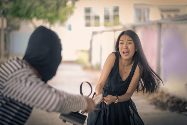 eine Person mit verdecktem Gesicht die einer jungen Frau die Handtasche aus der Hand reist 