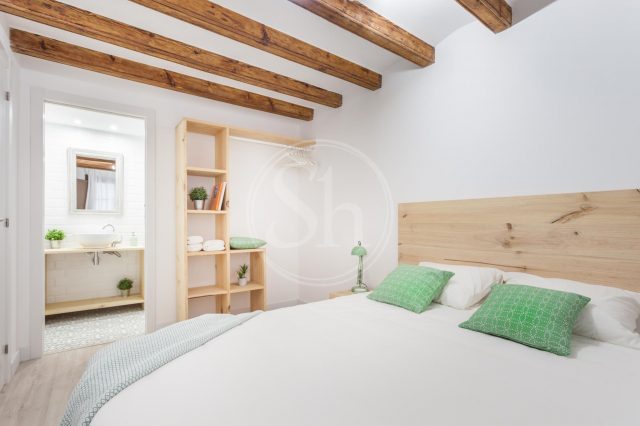 ein Schlafzimmer mit einem weiß bezogenem Bett, zwei grüne Kissen darauf und an der Wand steht ein Holzregal