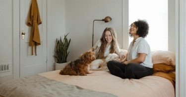 zwei Frauen auf einem Bett die fröhlich einen Hund streicheln