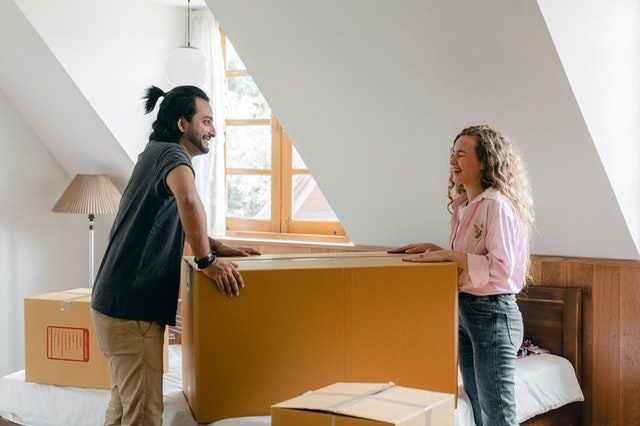 ein Pärchen in einer Wohnung, zwischen ihnen steht ein riesiger Umzugskarton