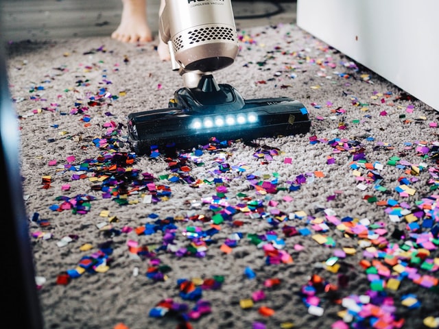 jemand der buntes Glitzerkonfetti von einem Teppich mit dem Staubsauger entfernt