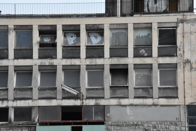 ein heruntergekommenes Gebäude von außen, einige Fenster sind kaputt und andere von Innen mit Grafiti besprüht