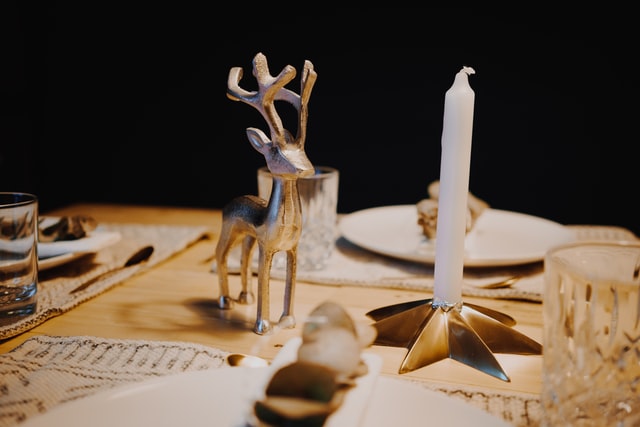 ein weihnachtlich gedeckter Holztisch mit einer weißen Kerze auf einem sternförmigen Kerzenständer und daneben eine silberne Rentierfigur 