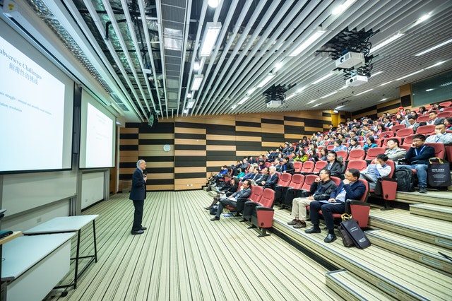 ein Vorlesungssaal in einer Universität mit roten stühlen und vielen Studenten die aufmerksam dem Profesor vorne zuhören