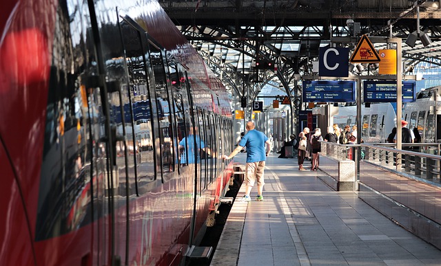 Bahnsteig an dem ein roter Zug gehalten hat und ein Man in blauem t-Shirt den Knopf drückt um die Tür zu öffnen