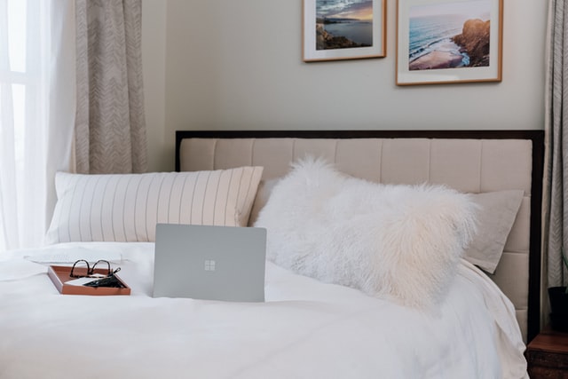 ein weiß bezogenes Bett mit einem grauen MacBook und einer schwarzen Brille darauf