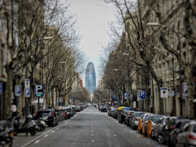 eine lange Straße Barcelonas mit geparkten Autos und Bäumen an beiden Straßenseiten und am Ende ist der Agbar Turm zu sehen