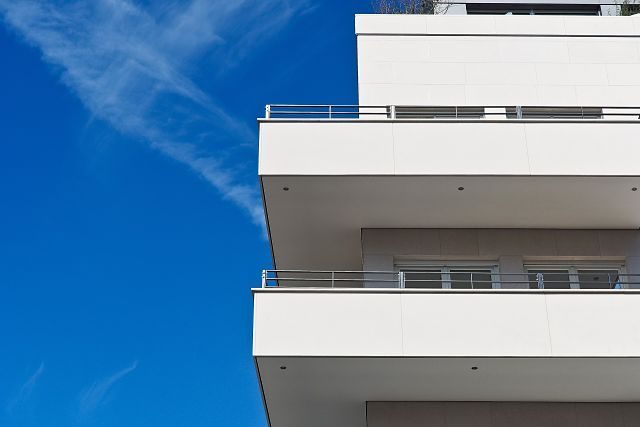 vor einem strahlend blauem Himmel sind die Ecken zweier Balkone eines weißen Hochhauses zu sehen