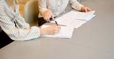 zwei Frauen mit weißen Blusen die an einem Tisch sitzen und einen Mietvertrag unterschreiben