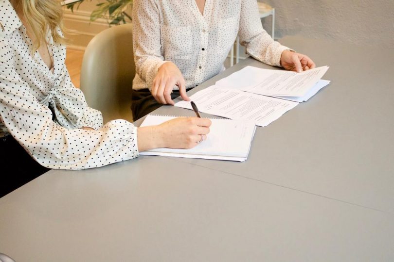 zwei Frauen mit weißen Blusen die an einem Tisch sitzen und einen Mietvertrag unterschreiben