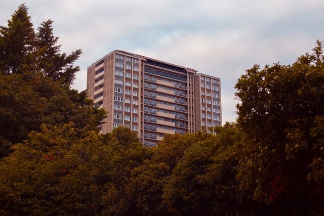 hinter mehreren Bäumen ist ein ziegelfarbiges Hochhaus zu sehen