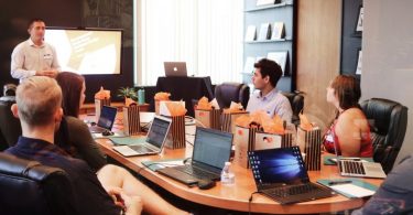 in einem Konferenzraum sitzen sechs sommerlich gekleidete Personen mit ihren Laptops