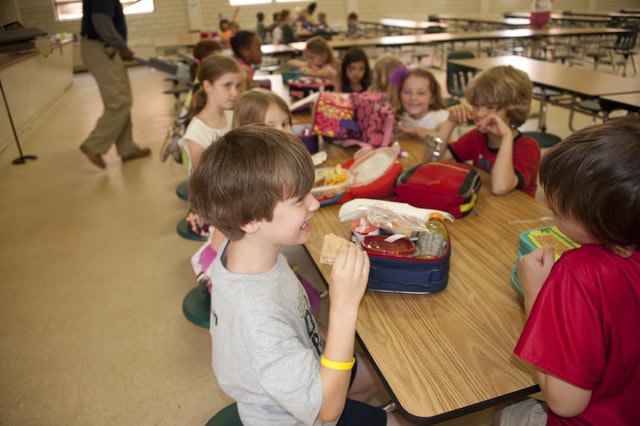 der Tisch einer Schulkantine an dem mehrere Schüler sitzen und fröhlich essen