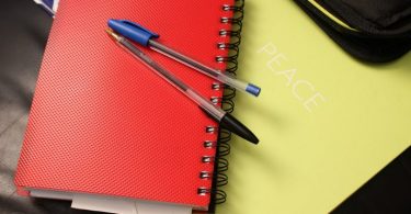 ein gelbes notizbuch auf dem ein rotes notizbuch auf dem ein blauer und ein schwarzer kugelschreiber liegen