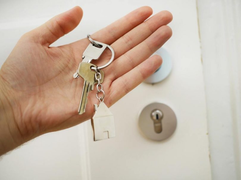 eine Hand mit einem Hausschlüssel vor einer weißen verschloßenen Tür